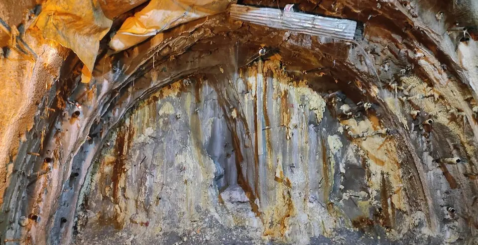 Wet, fractured rock at a railway tunnel face, streaked with water and grout